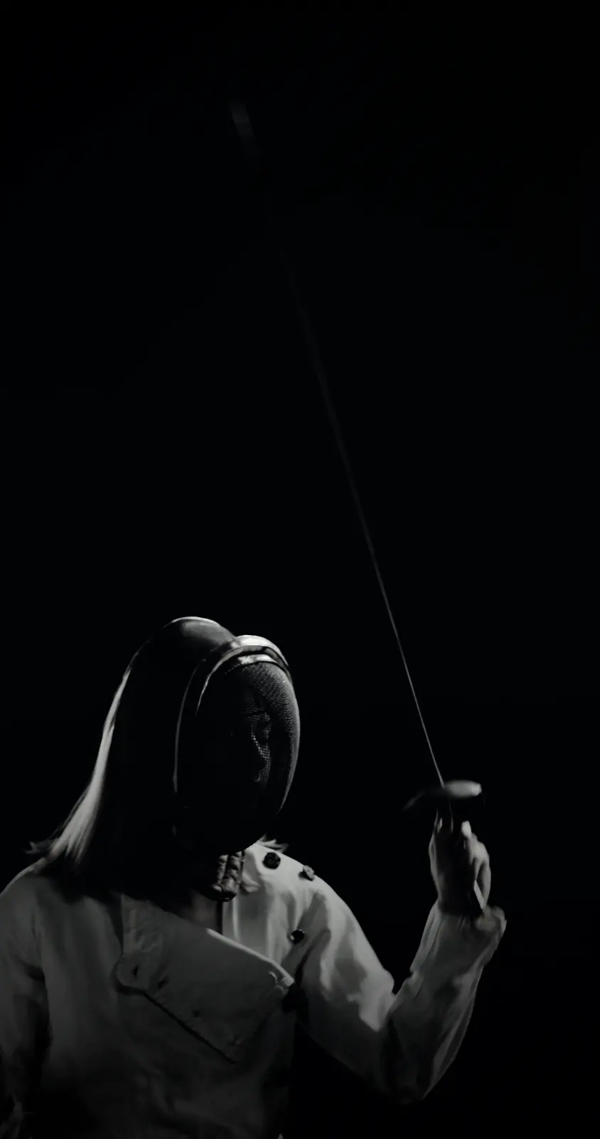 A masked fencer holding her foil upright