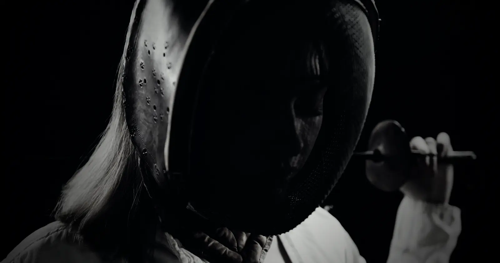 A fencer in her mask with the blade resting across her shoulders